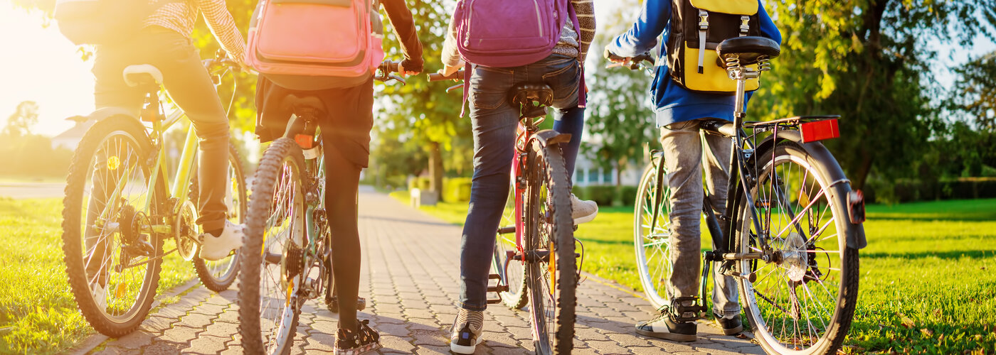 vier Kinder sitzen auf ihren Fahrrädern und stehen mit dem Rücken zur Kamera. Von vorne strahlt die Sonne durch die Reifen.