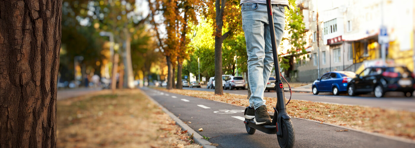 Ein junger Mann fährt mit dem E-Scooter auf einem Radweg.